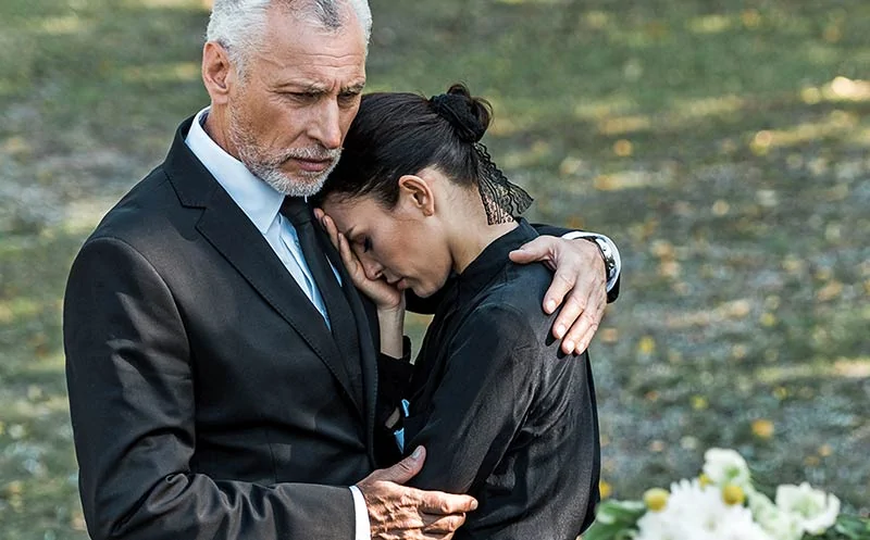 Ein Mann im Anzug tröstet eine Frau bei einer Beerdigung in der Elbmarsch, die wahrscheinlich von Bestatter Winsen geleitet wird. - Bestattungsunternehmen in Winsen, Harburg und in der Elbmarsch.